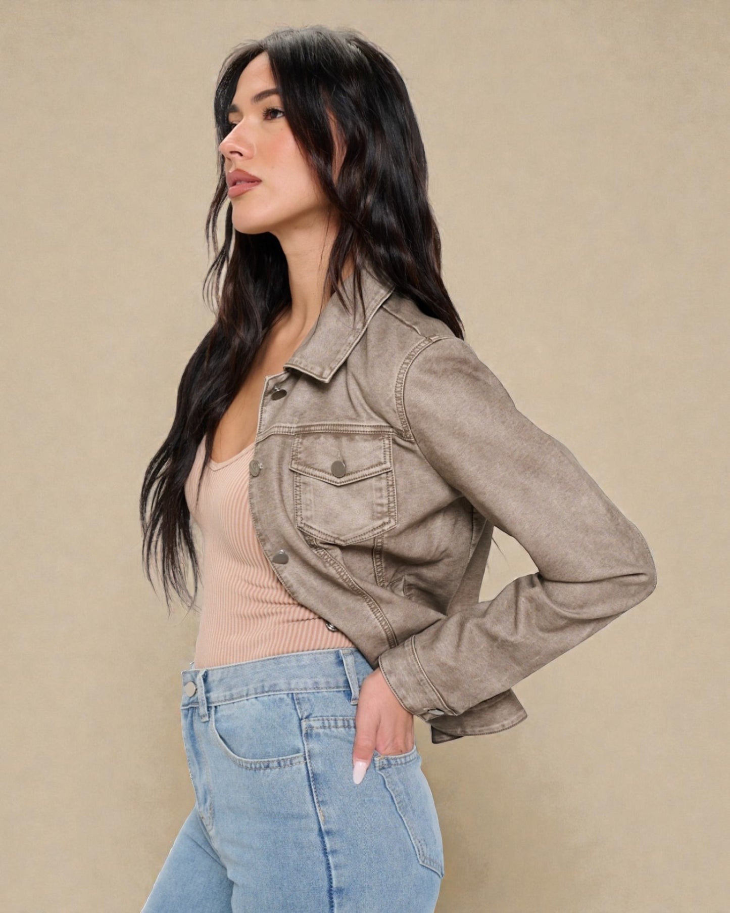 Woman wearing a beige denim jacket, pink top, and blue jeans against a beige background