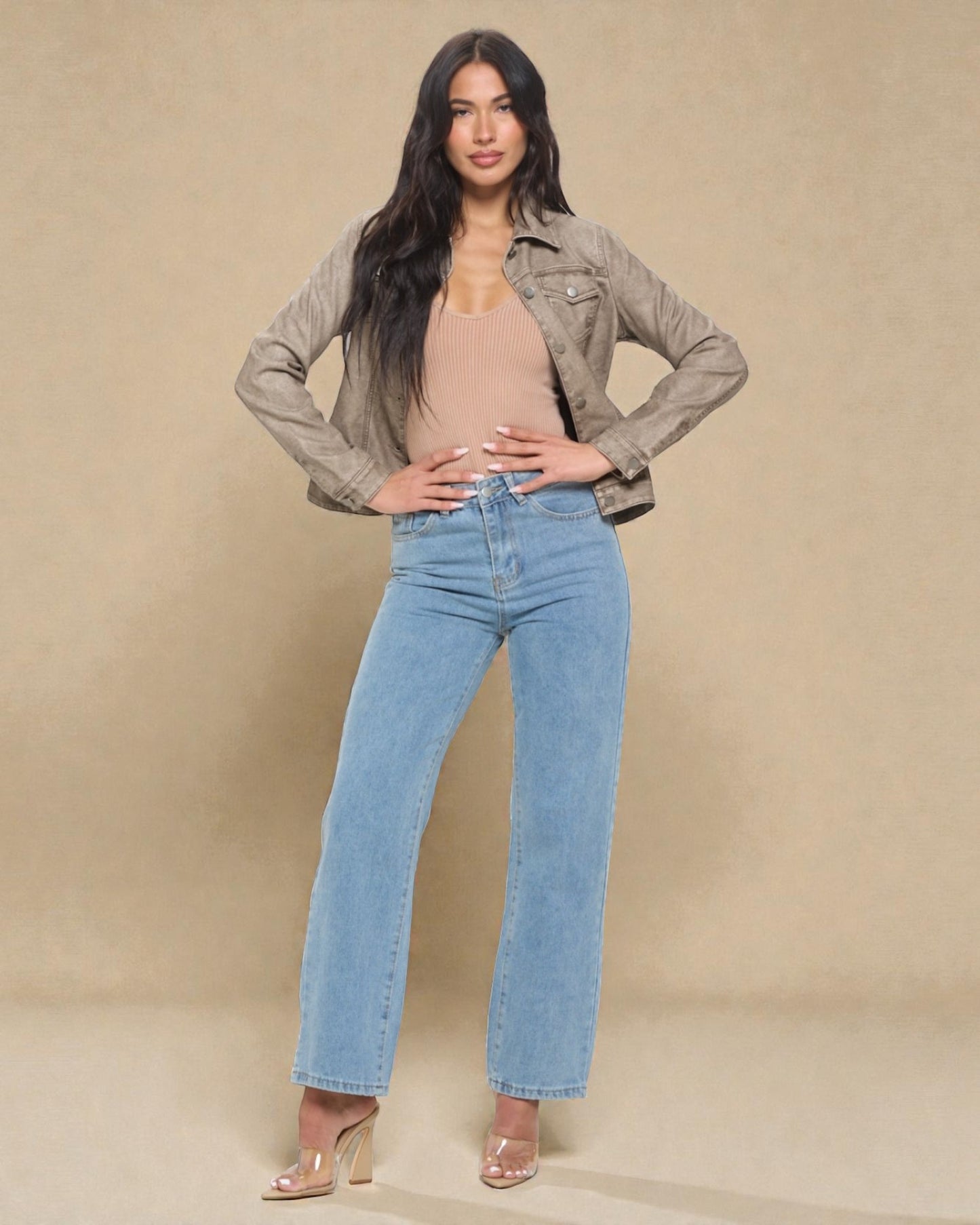Woman wearing a beige jacket, beige top, and blue jeans against a beige background