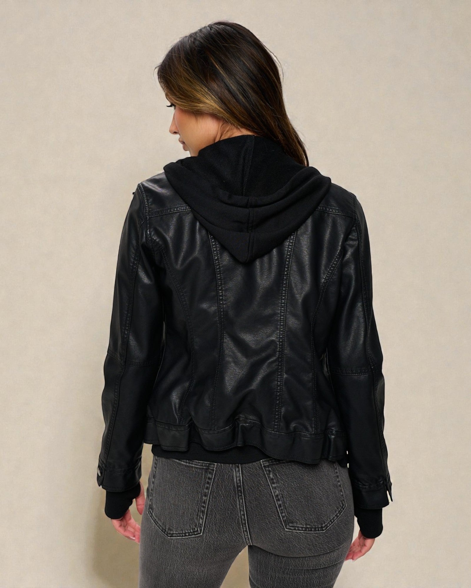 Person wearing a black leather jacket with a hood on a beige background