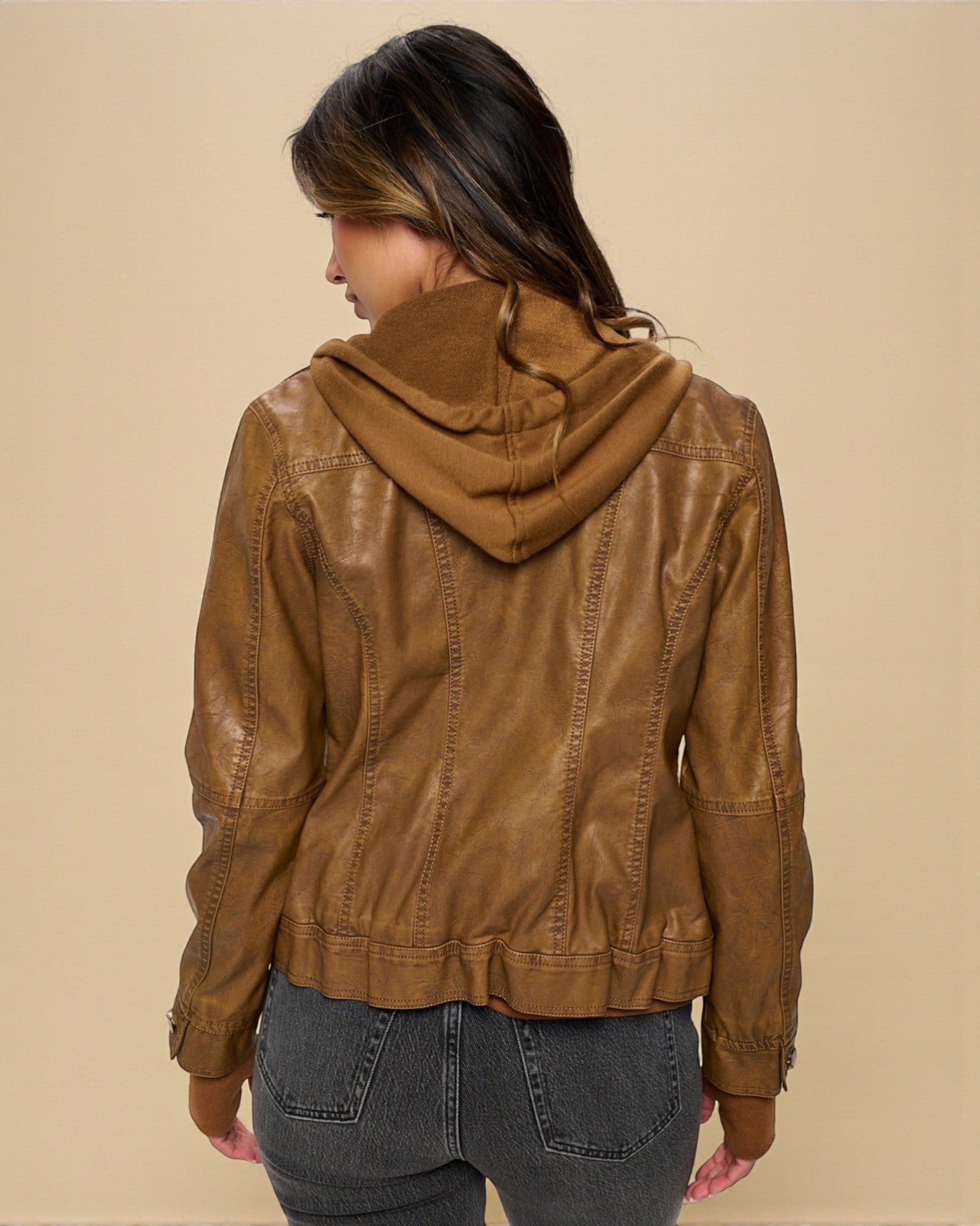 Person wearing a brown leather jacket with a hood on a beige background
