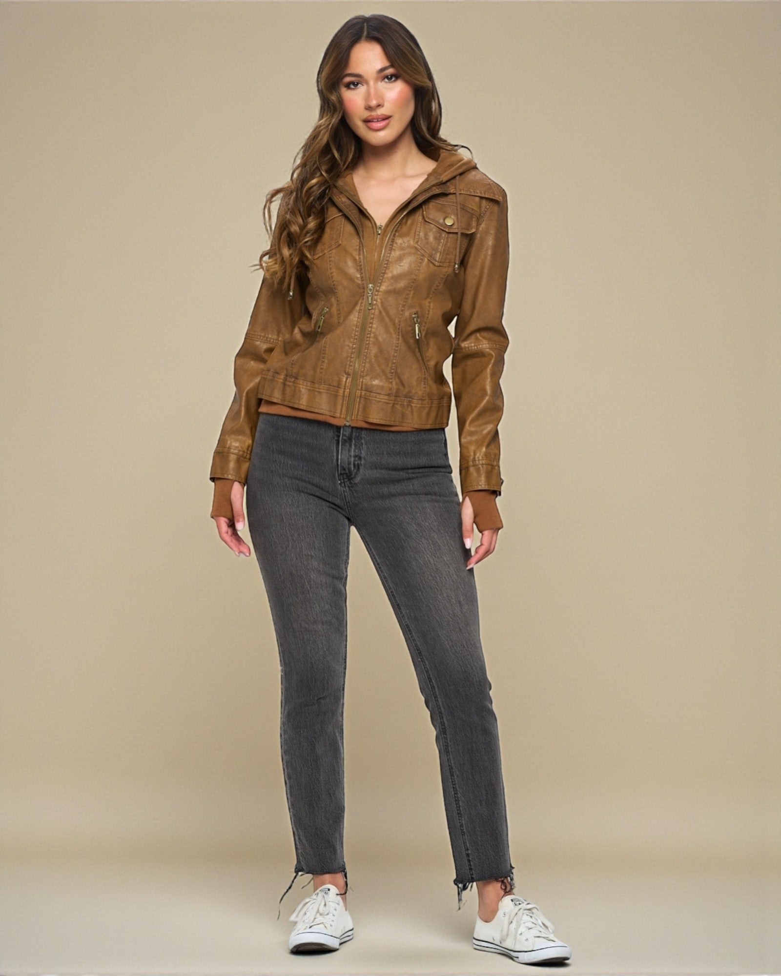 Woman wearing a brown leather jacket and gray jeans on a beige background