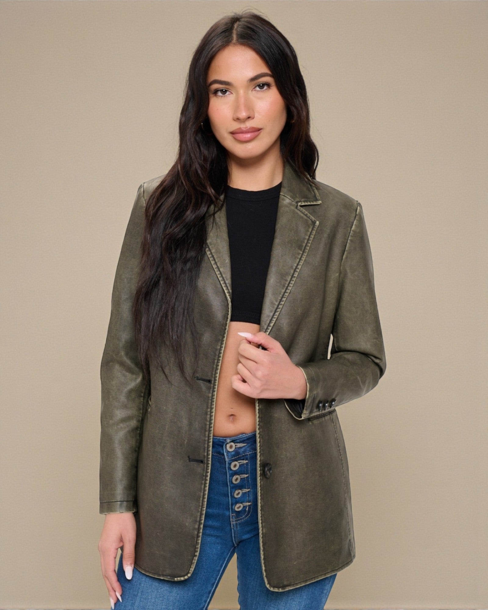 Woman wearing a green blazer over a black top and blue jeans on a beige background
