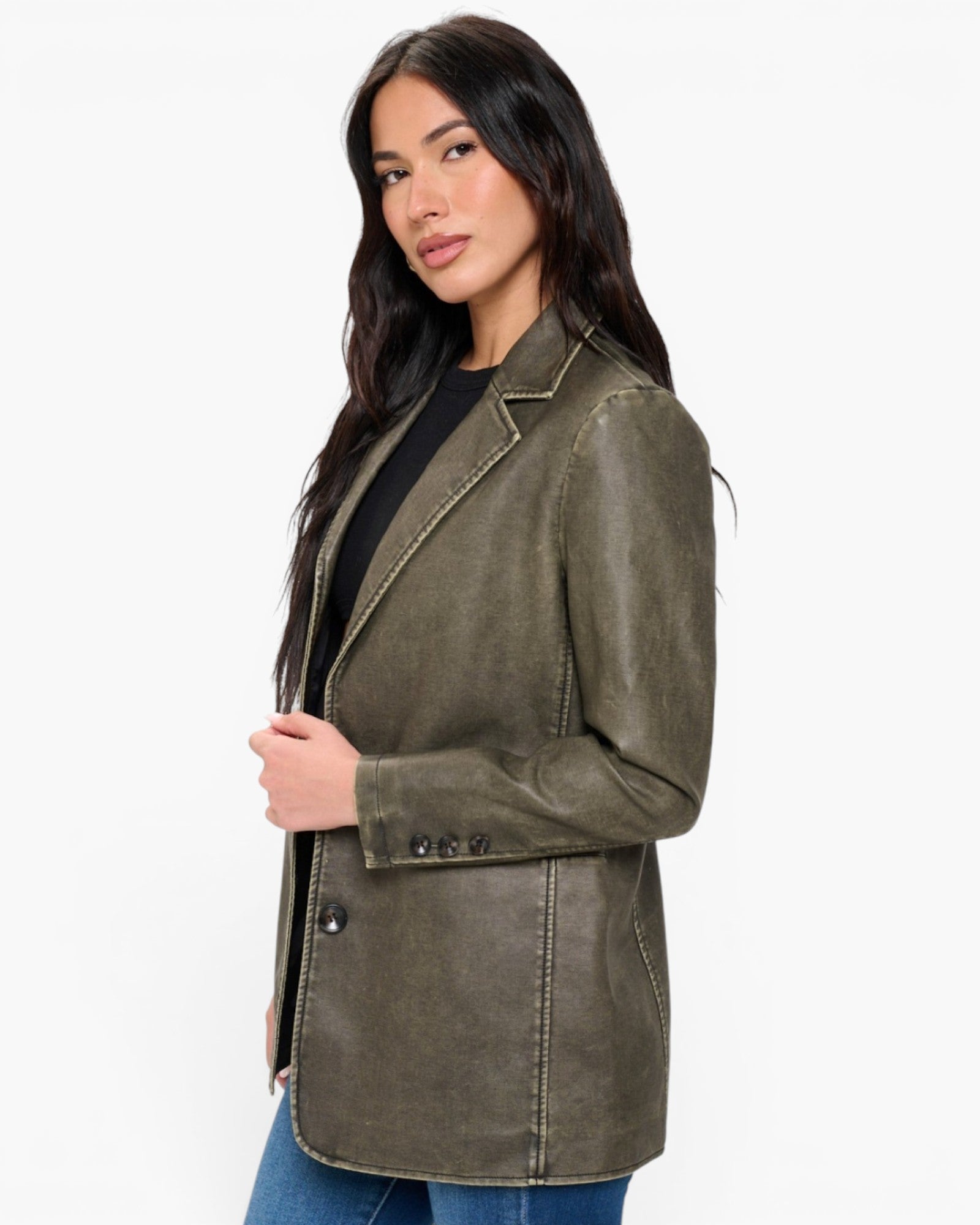 A woman modeling a double-breasted blazer in a washed olive green color, styled with a black top and blue jeans against a plain white background.