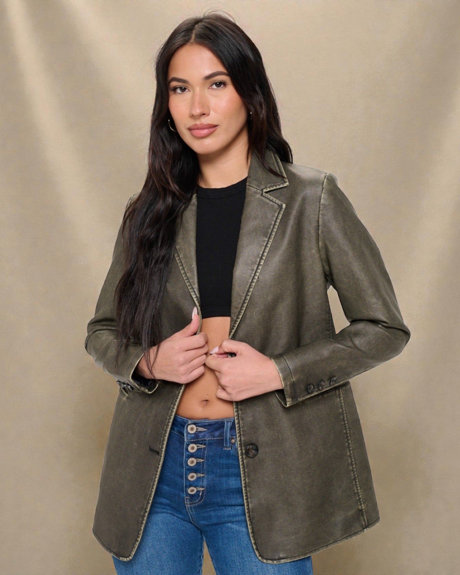 Woman wearing a green leather jacket over a black top and blue jeans on a beige background