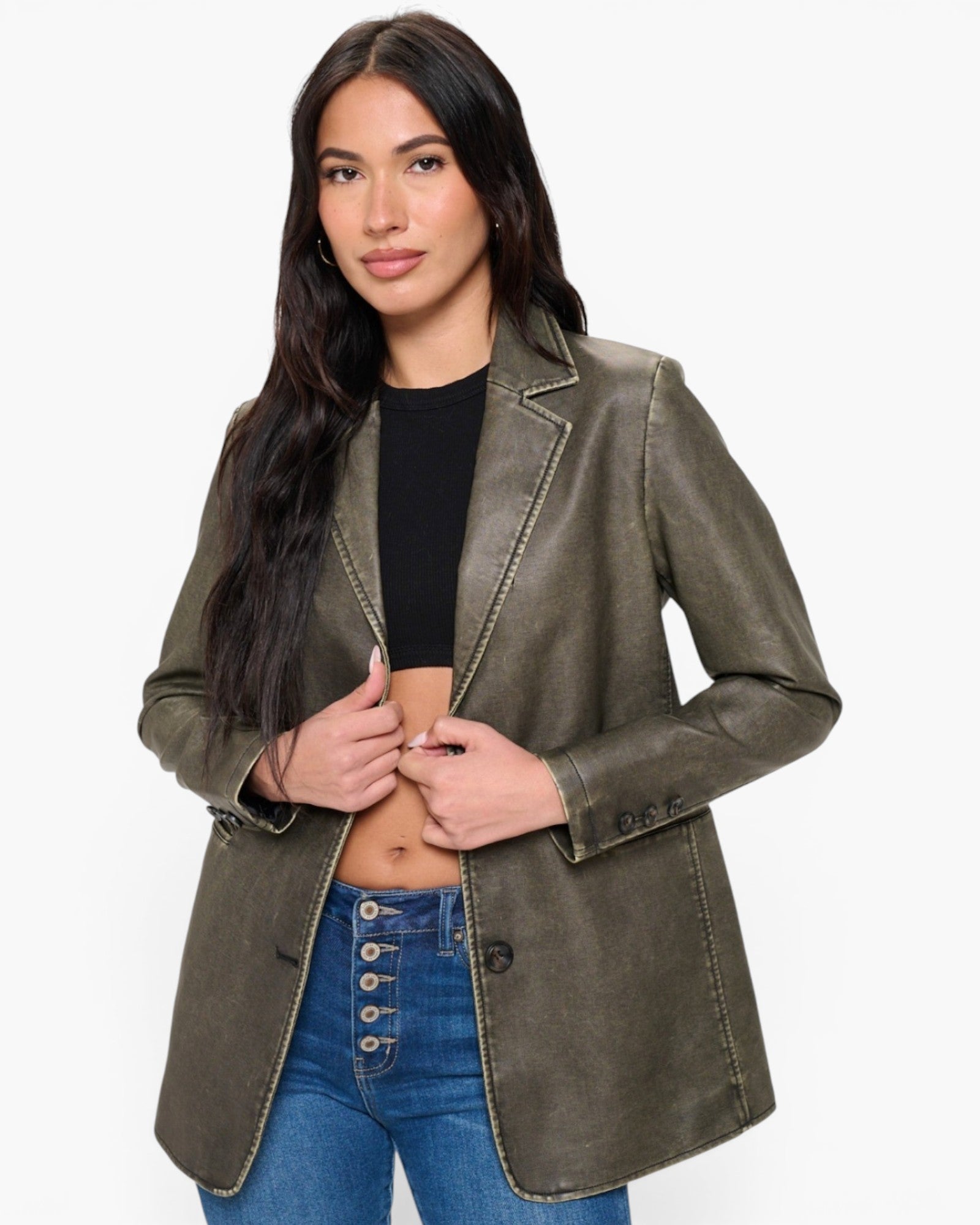 A woman modeling an olive green faux leather blazer with contrast stitching, worn over a black crop top and blue jeans against a plain white background.