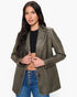 A woman modeling an olive green faux leather blazer with contrast stitching, worn over a black crop top and blue jeans against a plain white background.