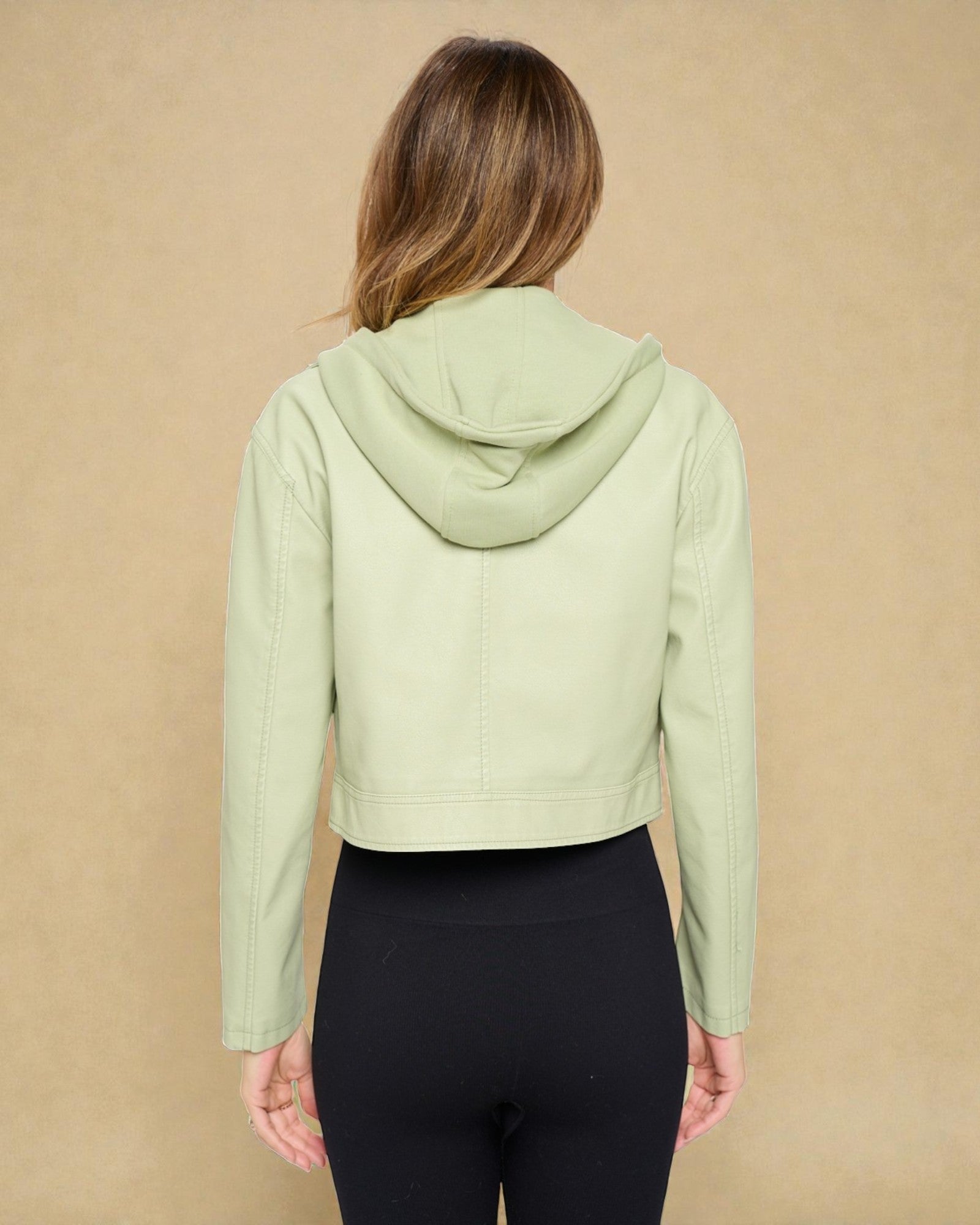 Person wearing a light green hoodie and black leggings against a beige background