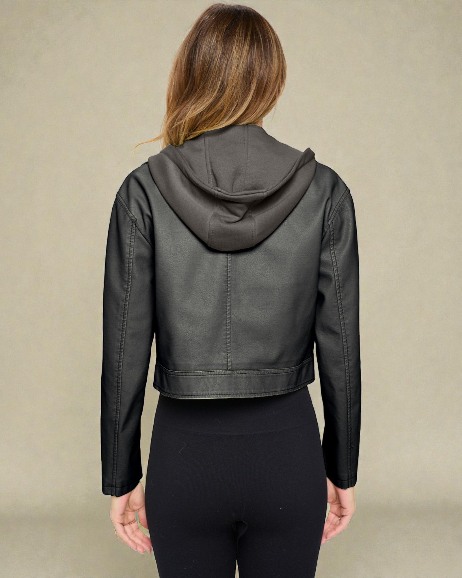 Person wearing a dark gray leather jacket with a hood on a beige background