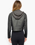 A woman viewed from the back wearing a dark gray faux-leather cropped hooded jacket and black leggings against a plain white background.