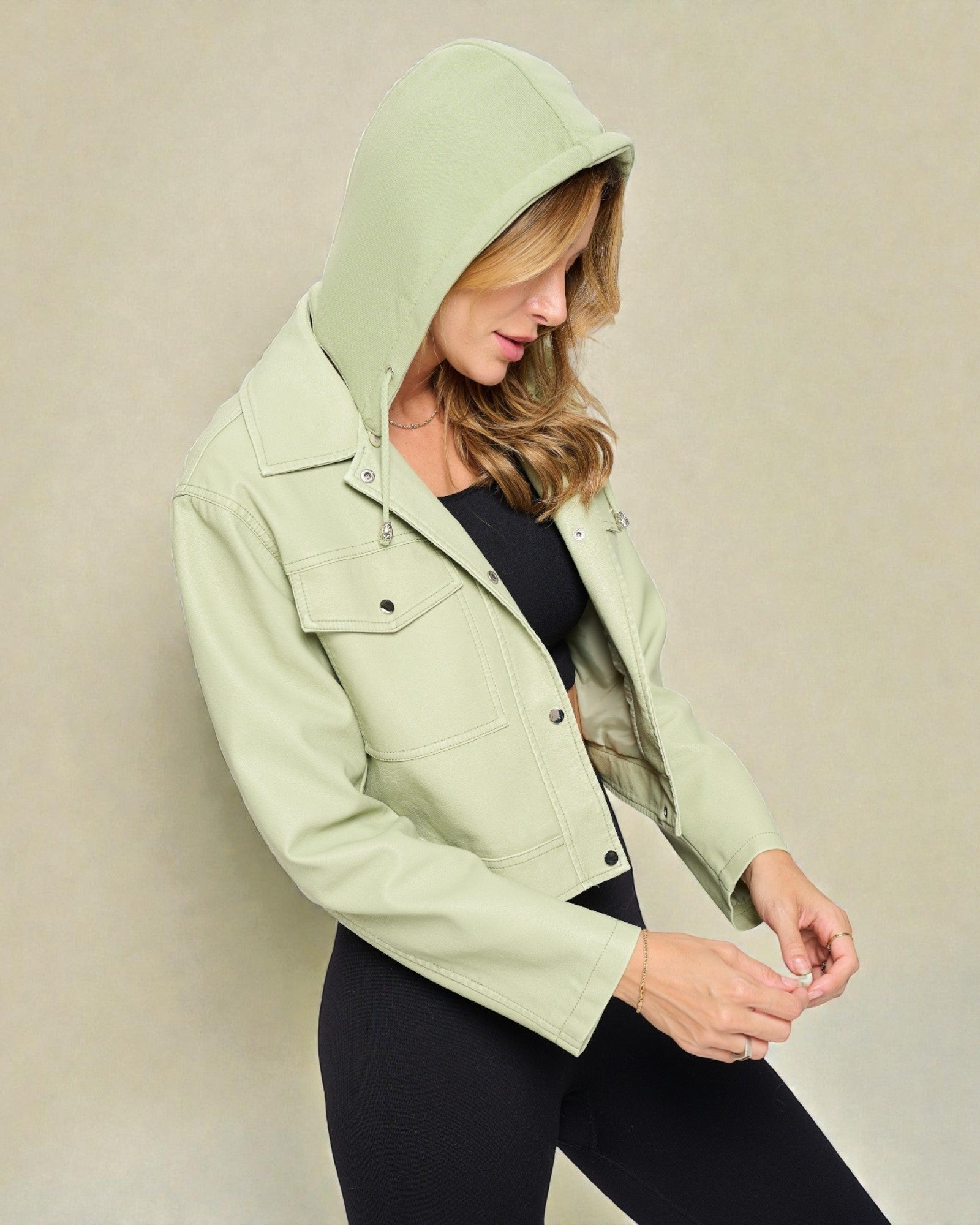 Person wearing a light green jacket with a hood against a beige background