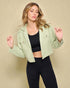 Woman wearing a light green jacket over a black top and leggings on a beige background