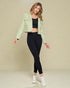 Woman wearing a light green jacket, black top, and leggings on a beige background