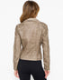 A woman viewed from the back wearing a cropped beige faux-leather jacket with silver studs on the shoulders, paired with black pants, against a plain white background.