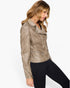 A woman wearing a taupe faux-suede moto jacket with studded shoulder details and black pants, photographed against a clean white studio background.