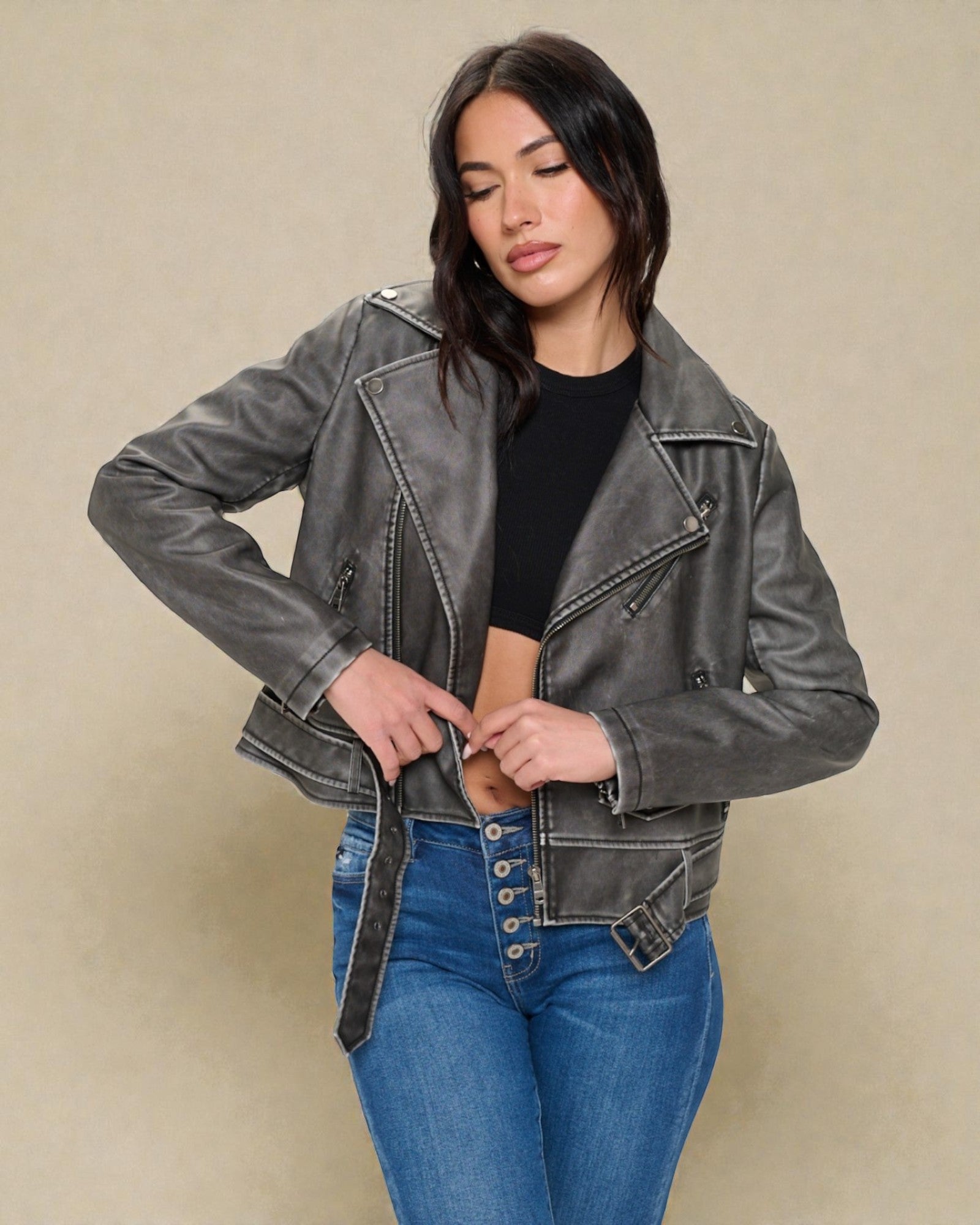 Woman wearing a gray denim jacket and blue jeans against a beige background