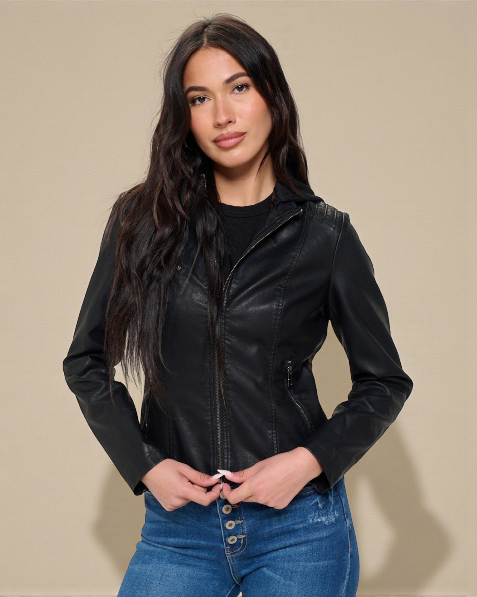 Woman wearing a black leather jacket and blue jeans against a beige background