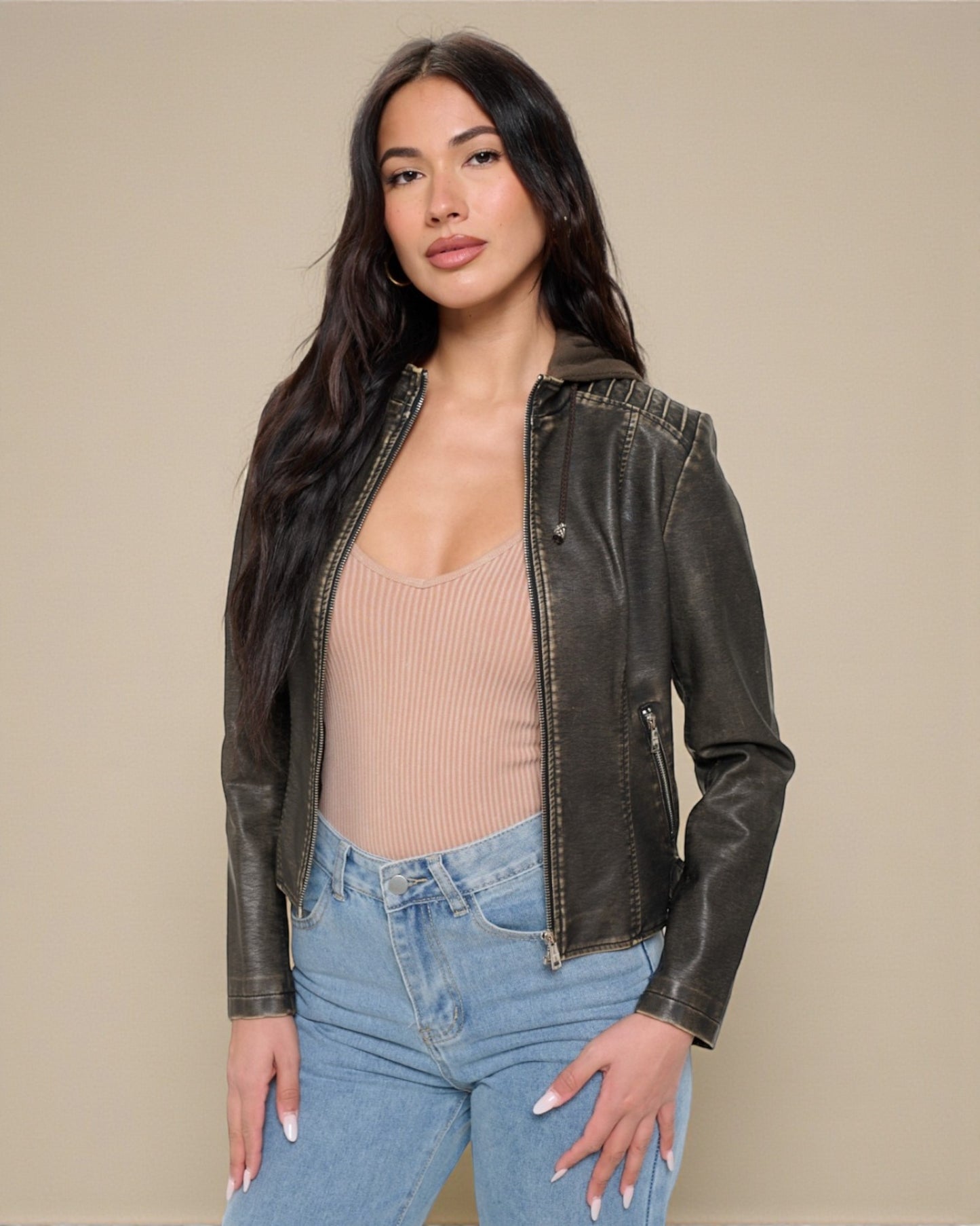 Woman wearing a brown leather jacket over a beige top and blue jeans on a beige background