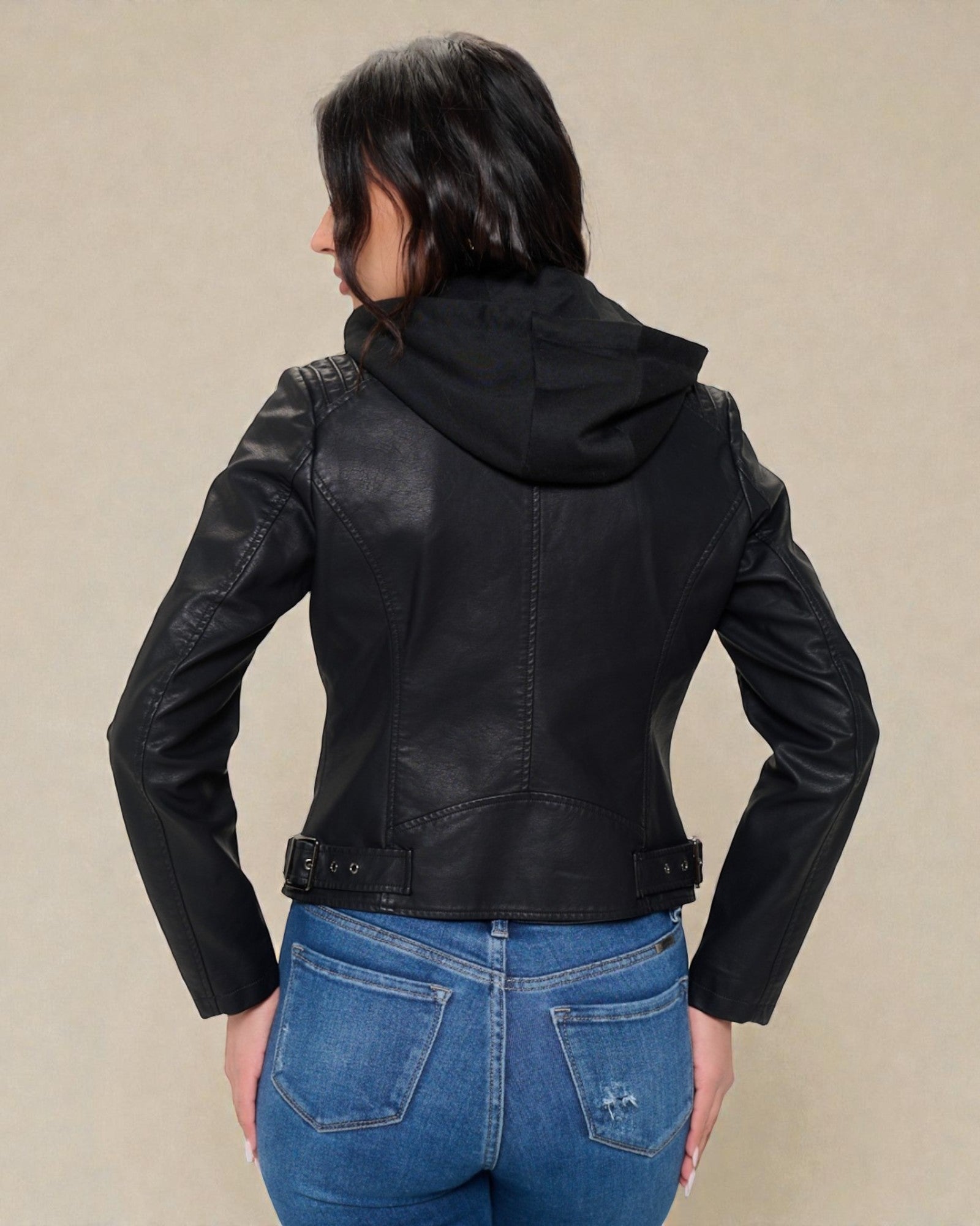 Person wearing a black leather jacket with a hood on a beige background