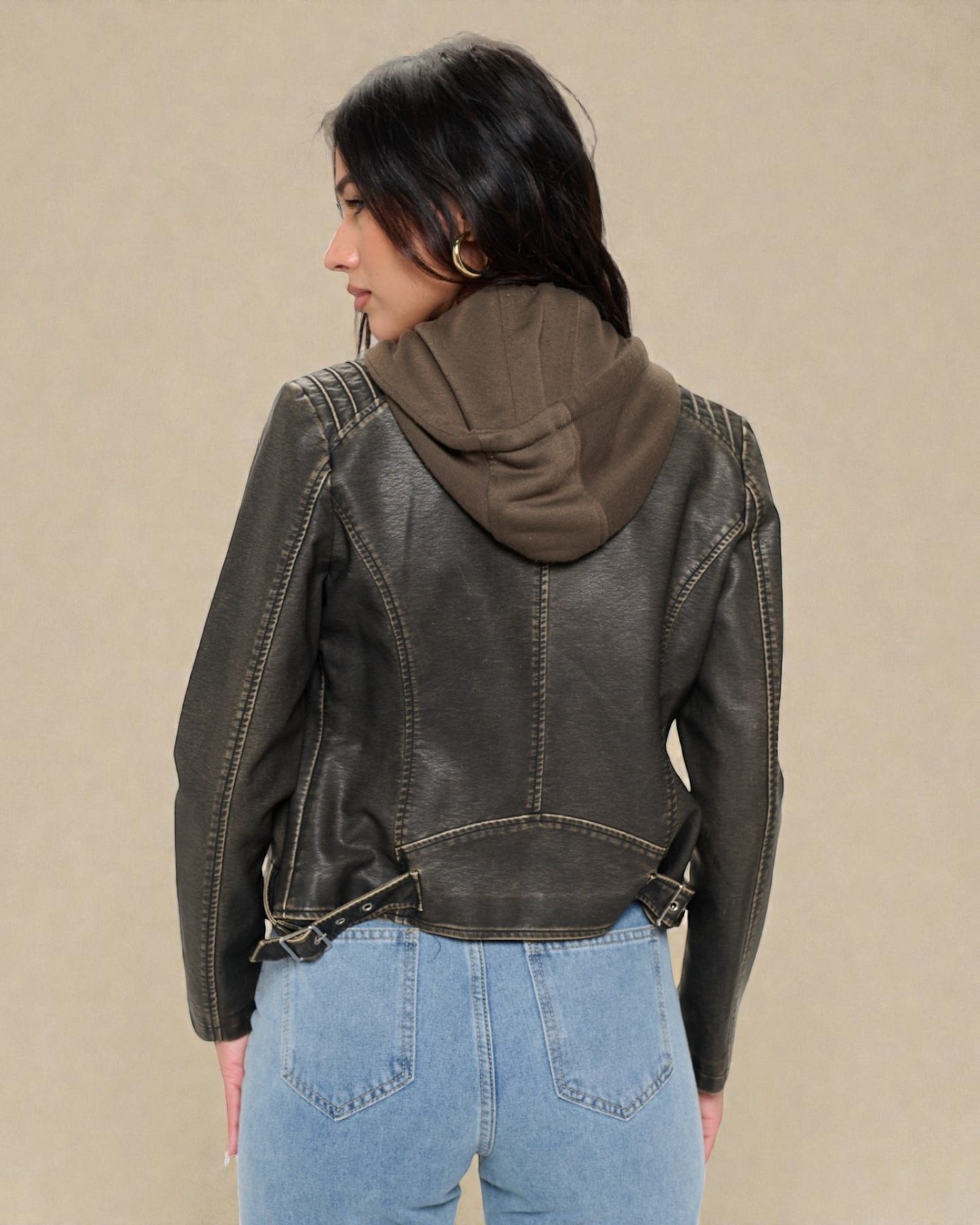 Person wearing a dark leather jacket with a hood against a beige background