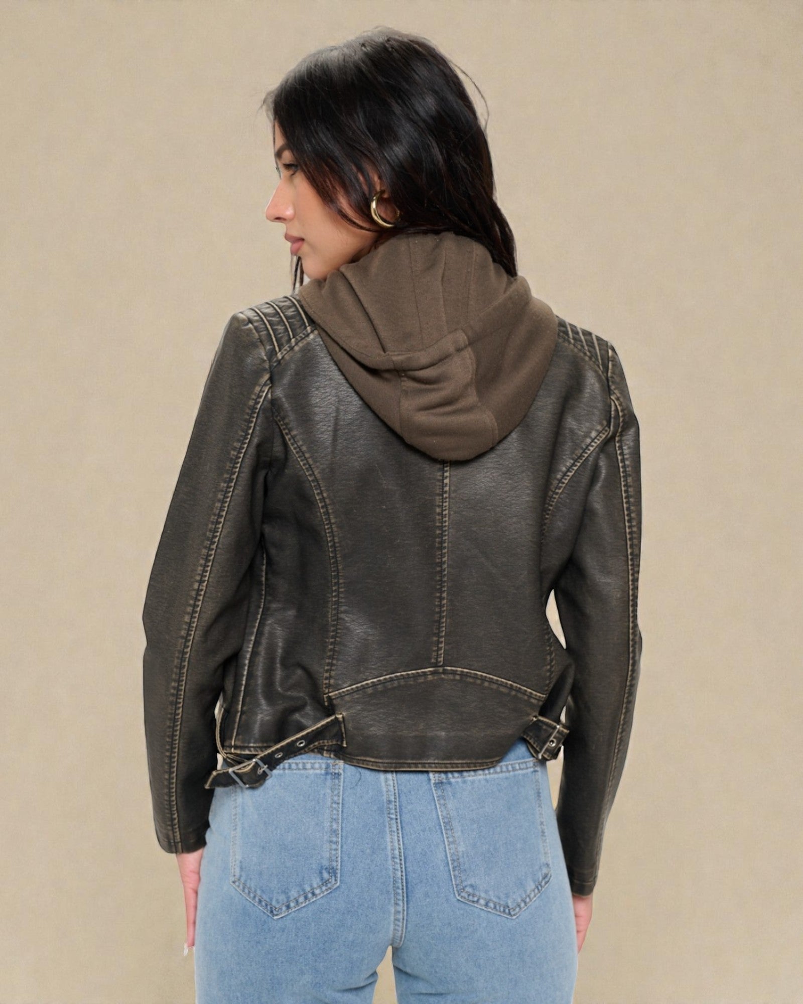 Person wearing a dark leather jacket with a hood against a beige background