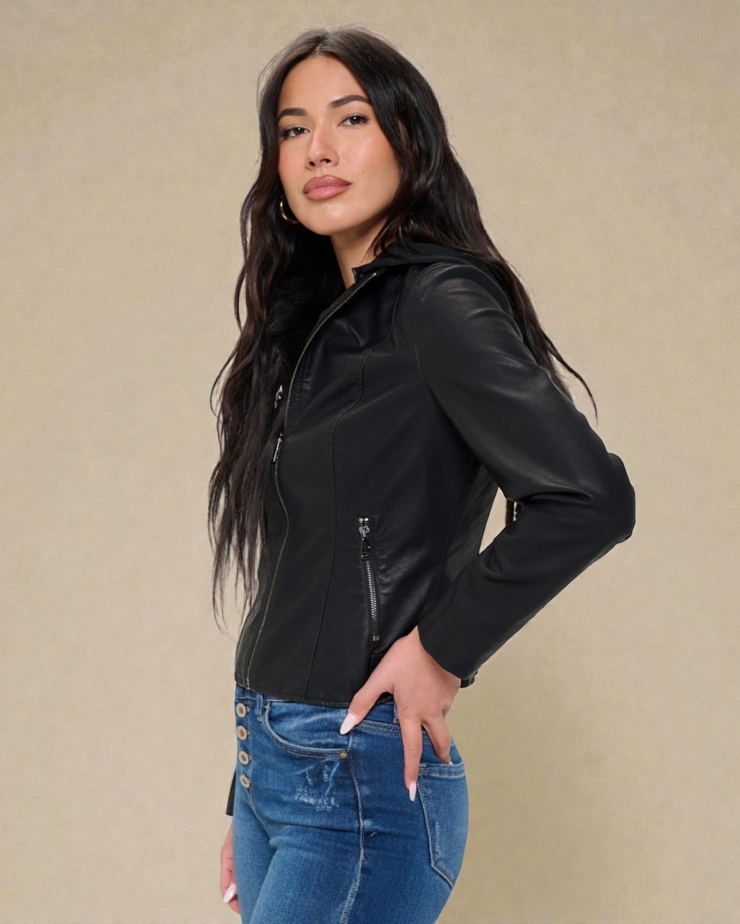 Woman wearing a black leather jacket and blue jeans against a beige background