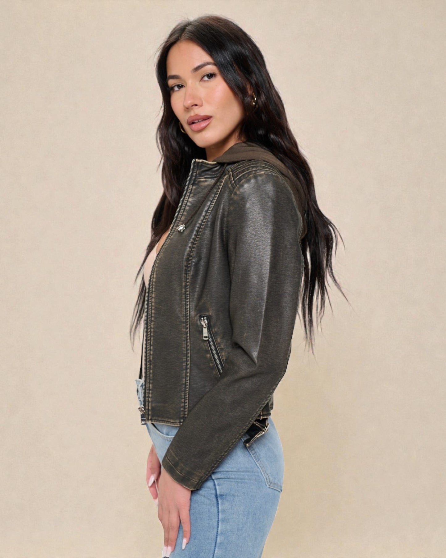 Woman wearing a dark green leather jacket and light blue jeans on a beige background