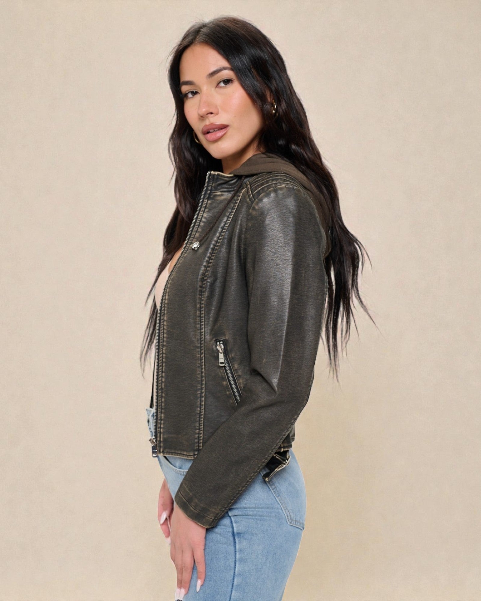 Woman wearing a dark green leather jacket and light blue jeans on a beige background