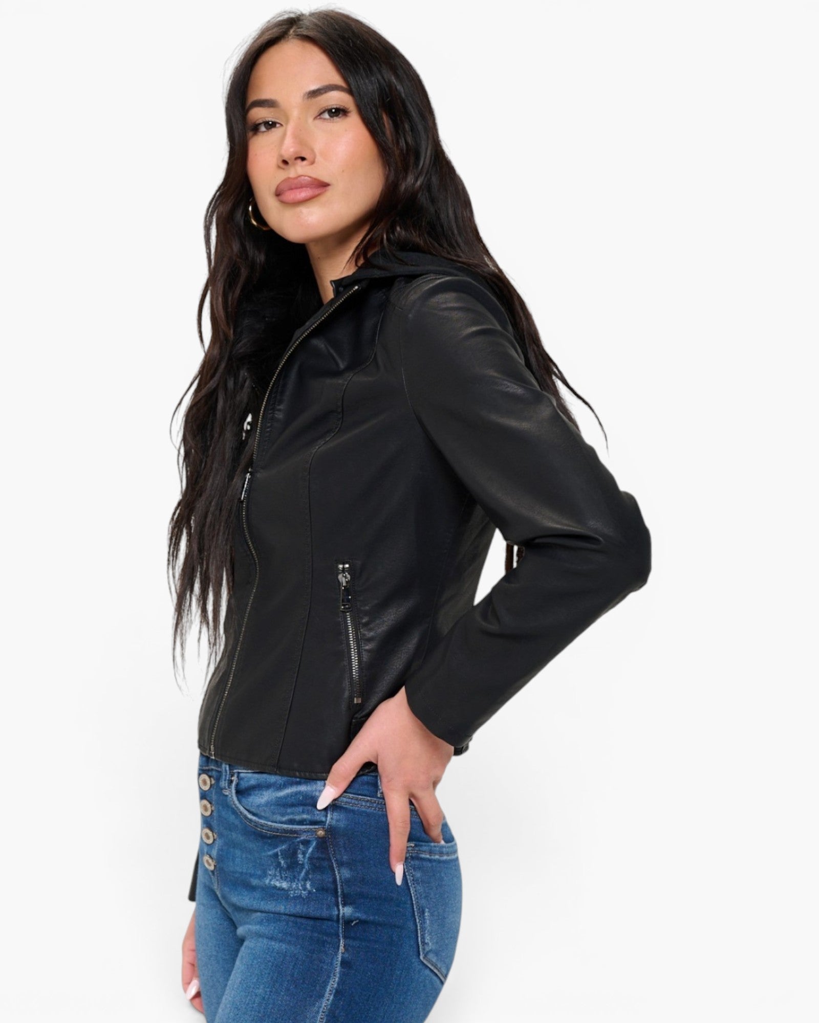 A woman modeling a black faux-leather moto jacket with a high collar and zippered front, paired with blue jeans, against a plain white background.