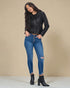 Woman wearing a black leather jacket, blue jeans, and black boots on a beige background