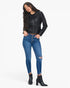 A woman modeling a black faux-leather zip-up jacket, blue high-waisted skinny jeans with distressed details, and black ankle boots against a plain white background.