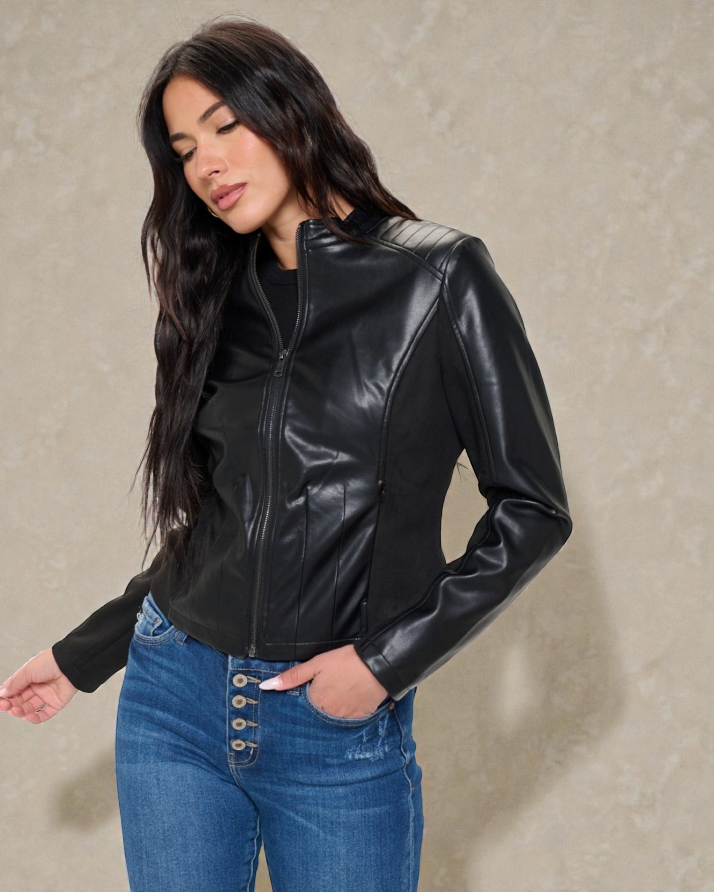Woman wearing a black leather jacket and blue jeans against a beige background