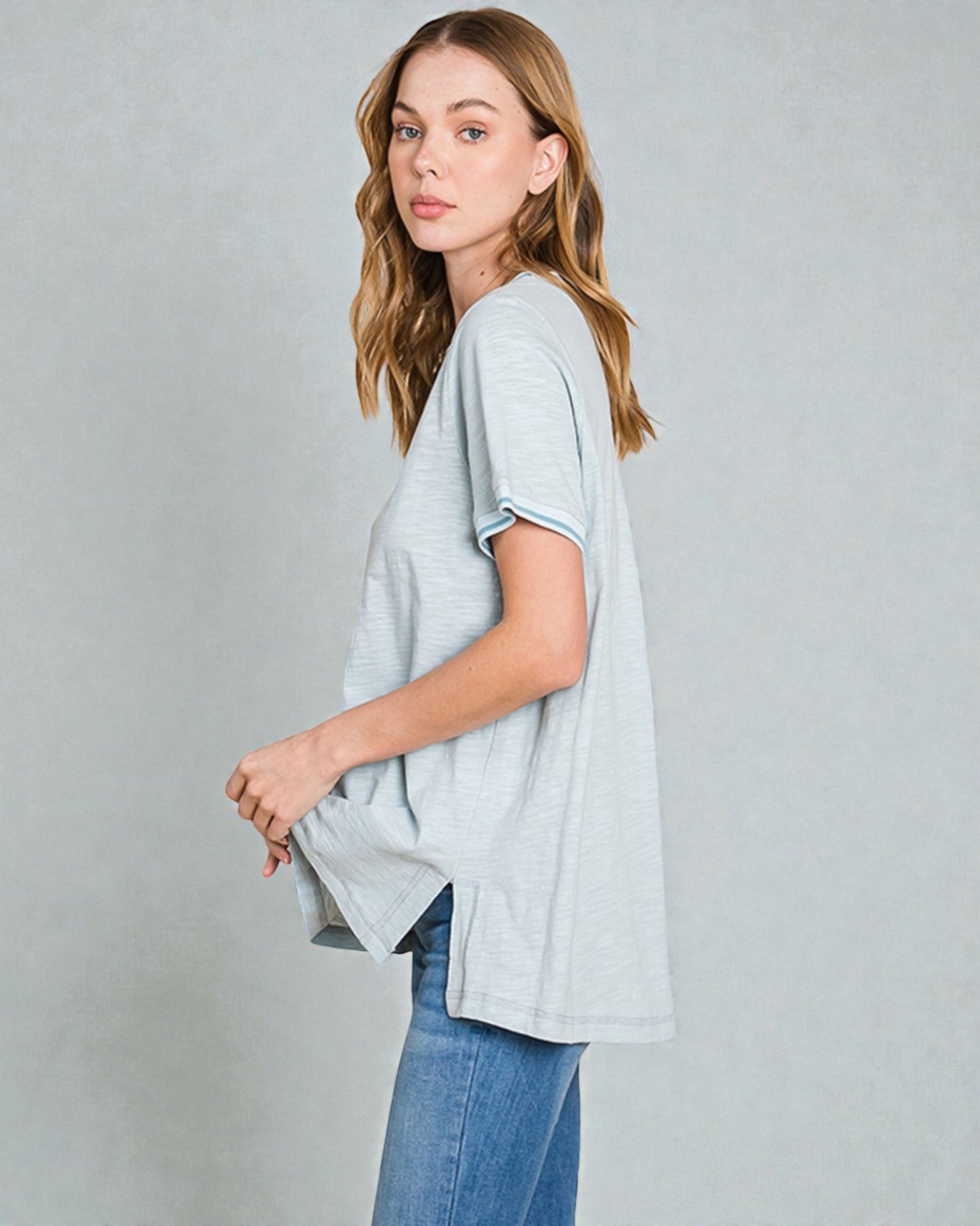 Woman wearing a light gray oversized t-shirt and blue jeans on a plain background