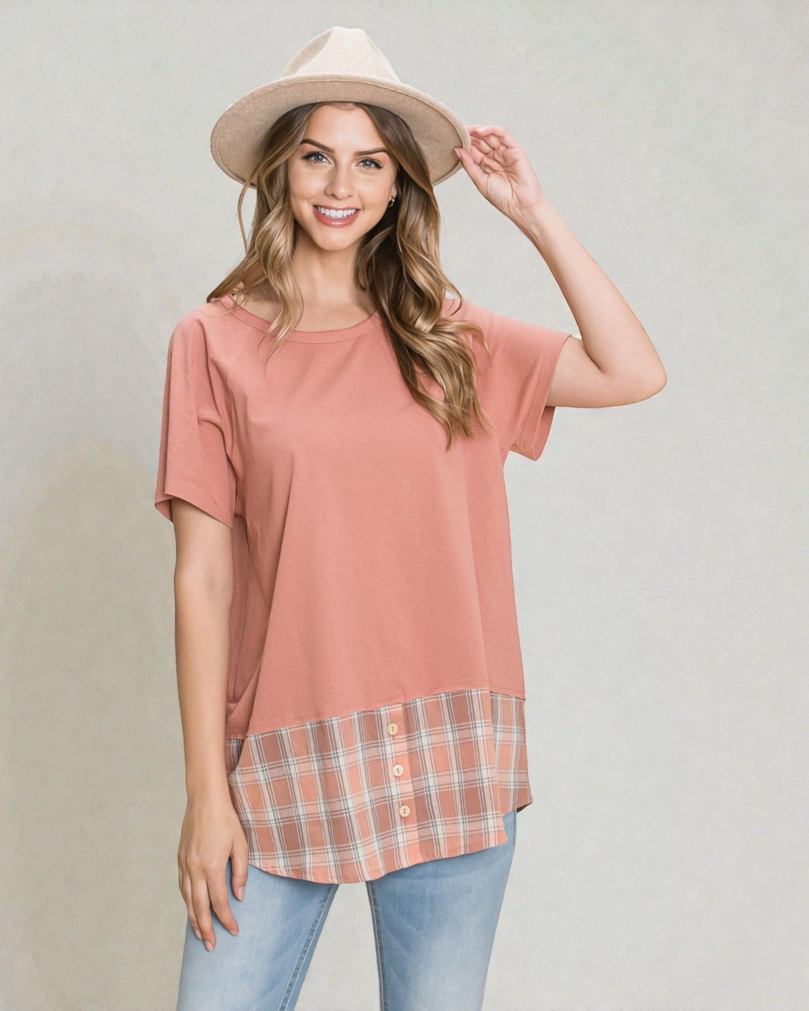 Woman wearing a pink top with plaid bottom and beige hat on a plain background