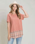 Woman wearing a pink top with plaid bottom and beige hat on a plain background