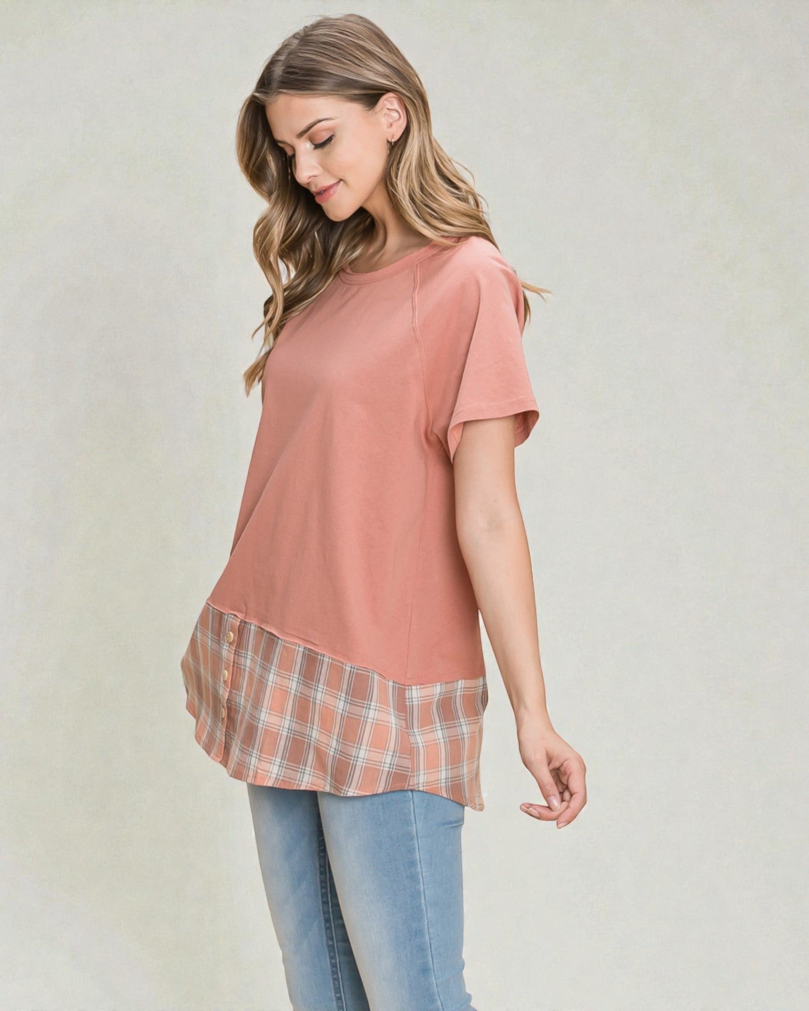 Woman wearing a pink top with plaid trim and blue jeans on a plain background