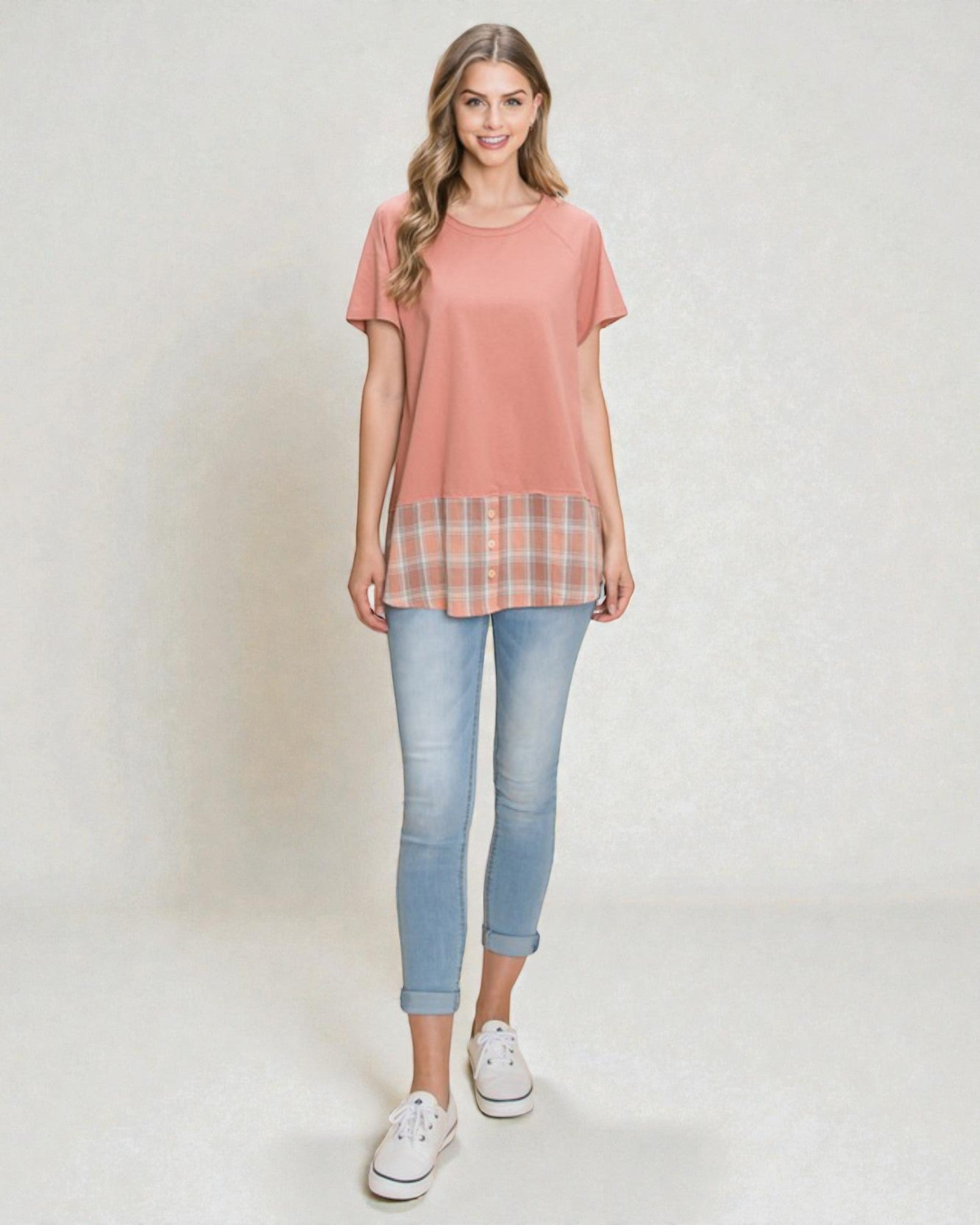 Woman wearing a coral t-shirt with a plaid layer and light blue jeans on a white background