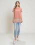 Woman wearing a coral t-shirt with a plaid layer and light blue jeans on a white background