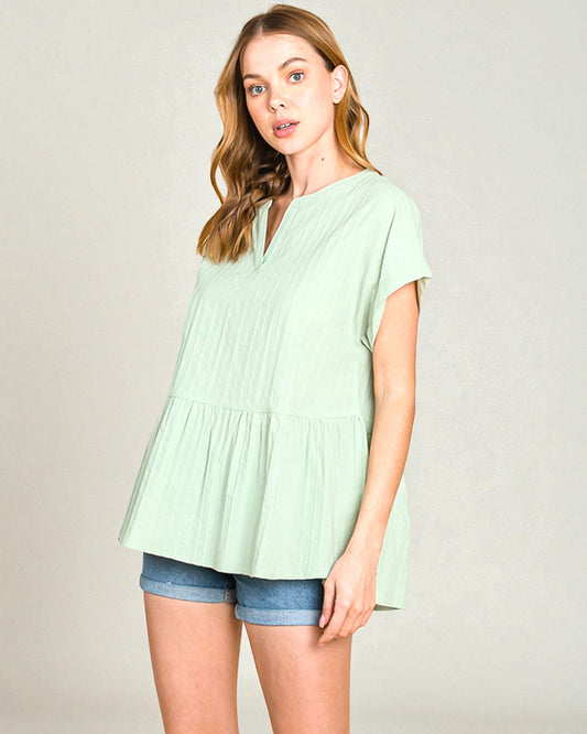 Woman wearing a light green blouse and denim shorts against a plain background