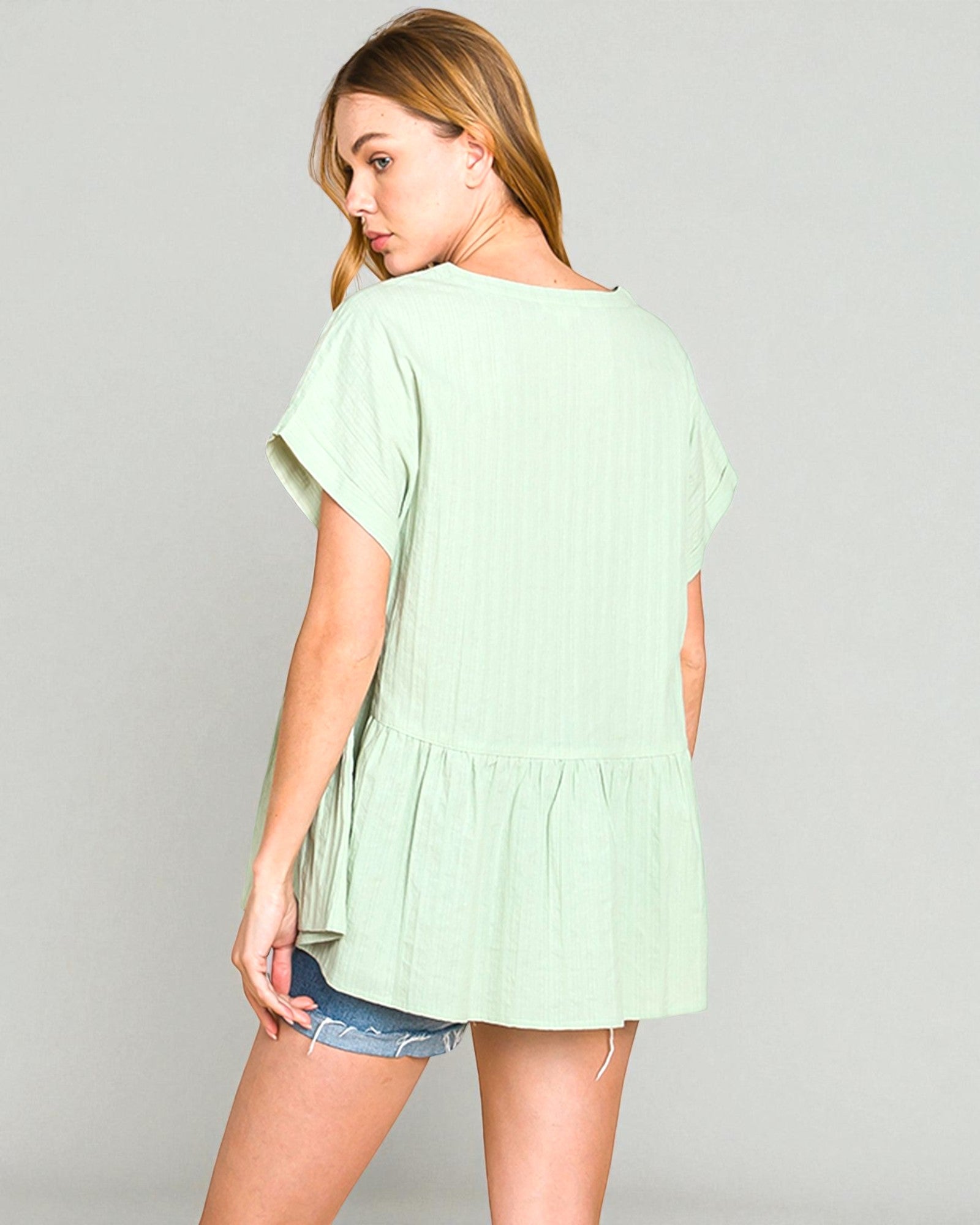 Woman wearing a light green blouse with ruffled sleeves on a gray background