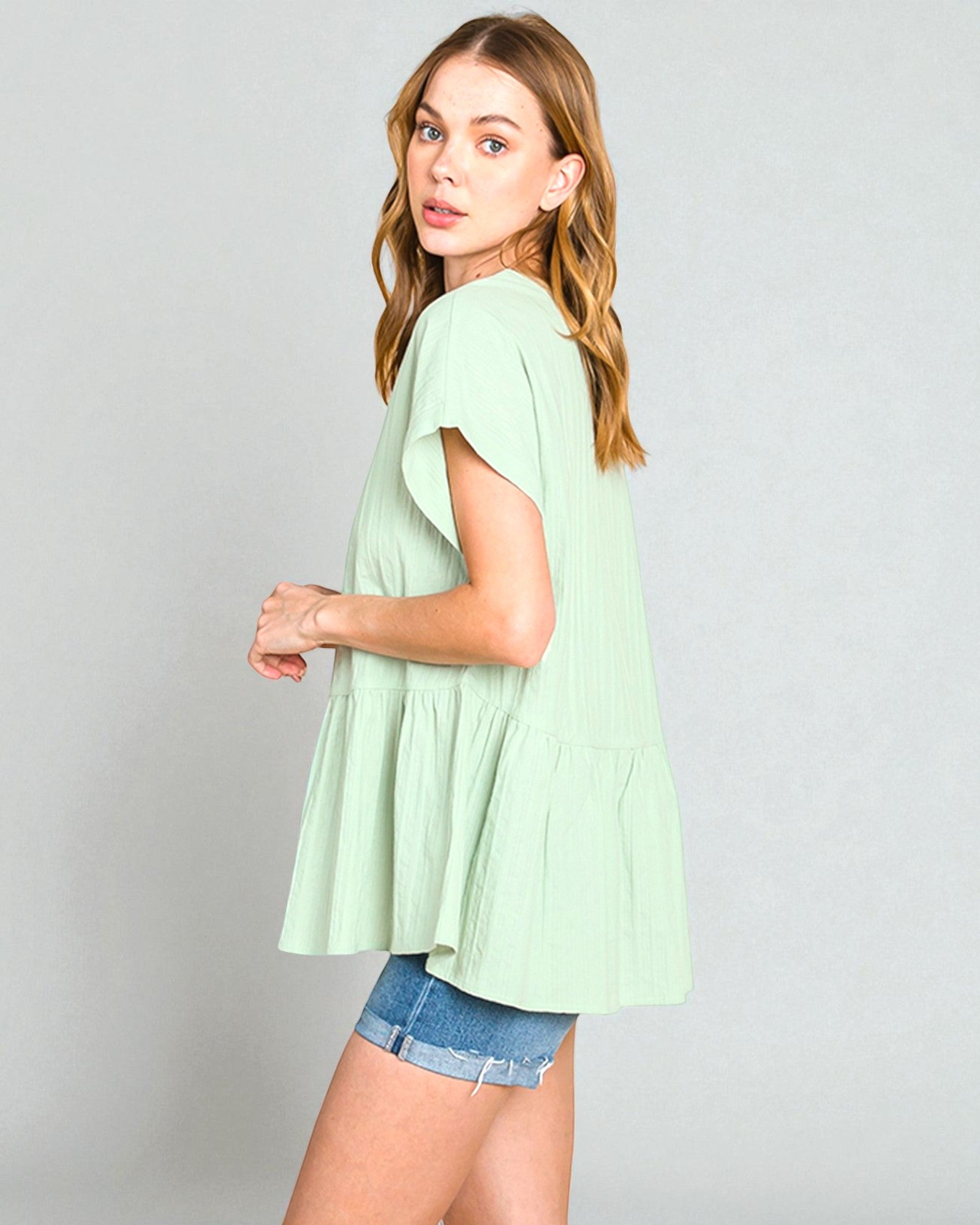 Woman wearing a light green top and denim shorts on a gray background