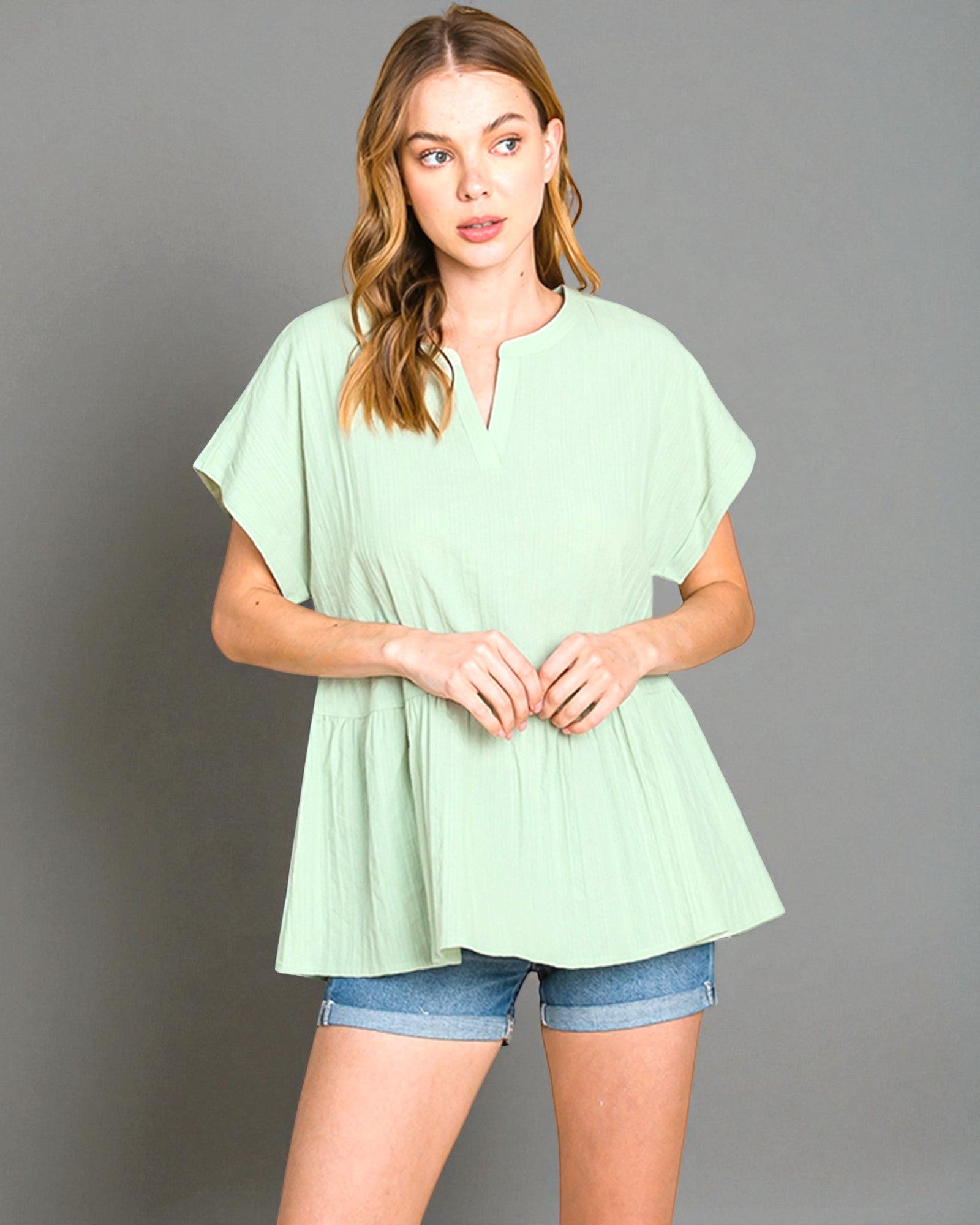 Woman wearing a light green top and denim shorts on a gray background