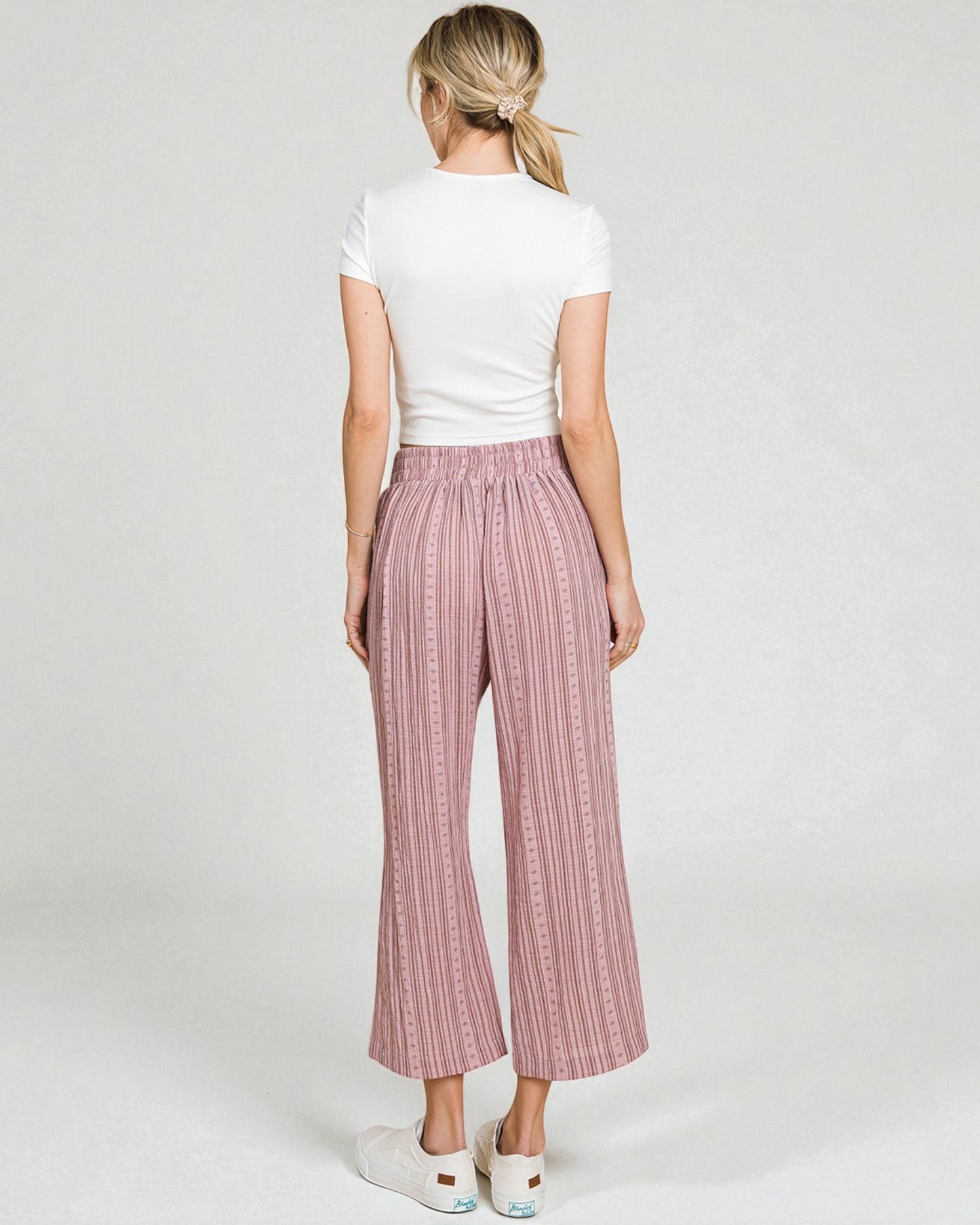 Woman wearing pink checkered pants and a white top on a plain background