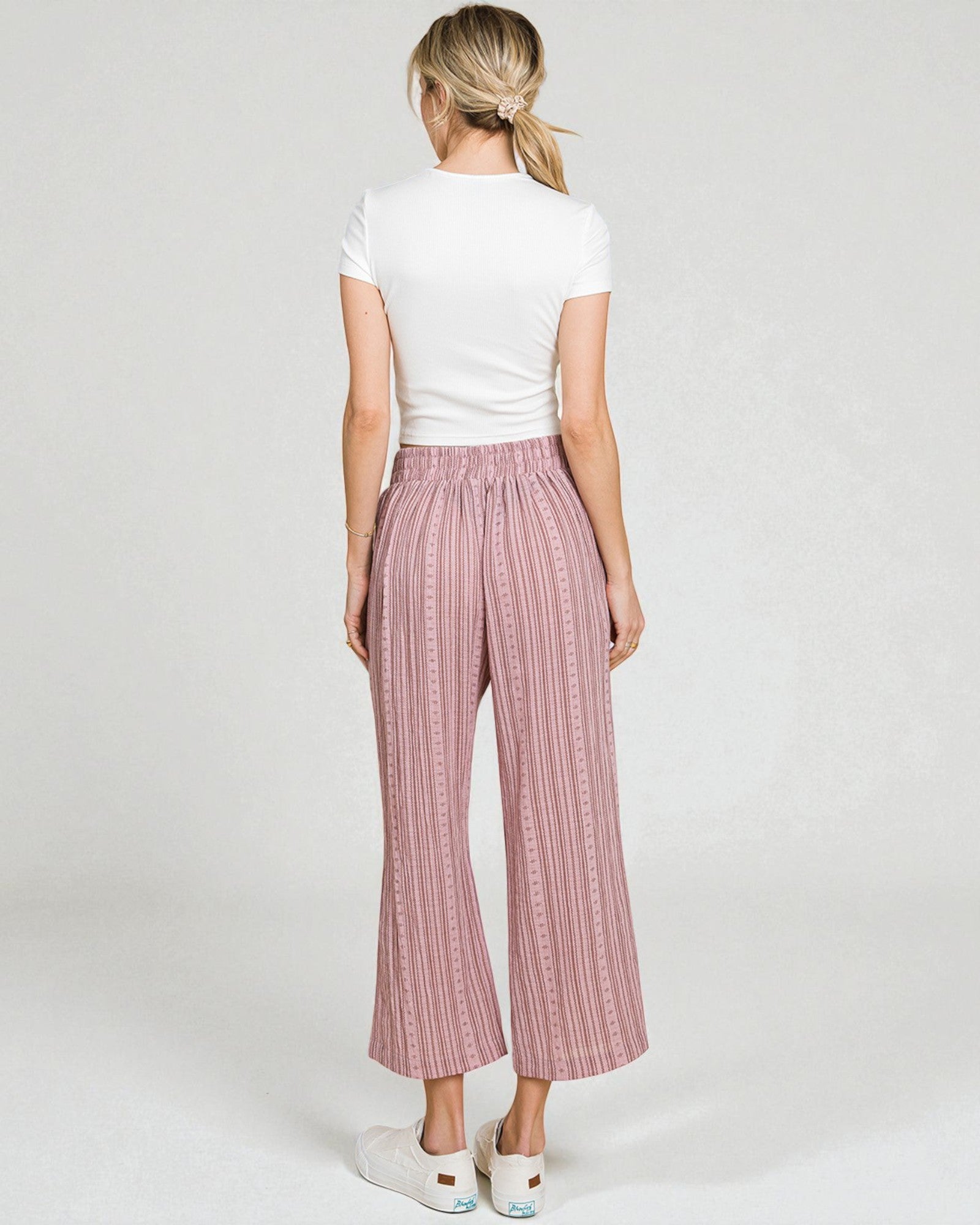 Woman wearing pink checkered pants and a white top on a plain background