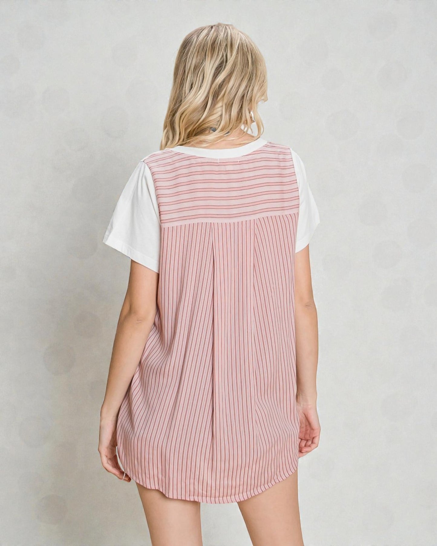 Person wearing a pink striped dress over a white shirt on a plain background