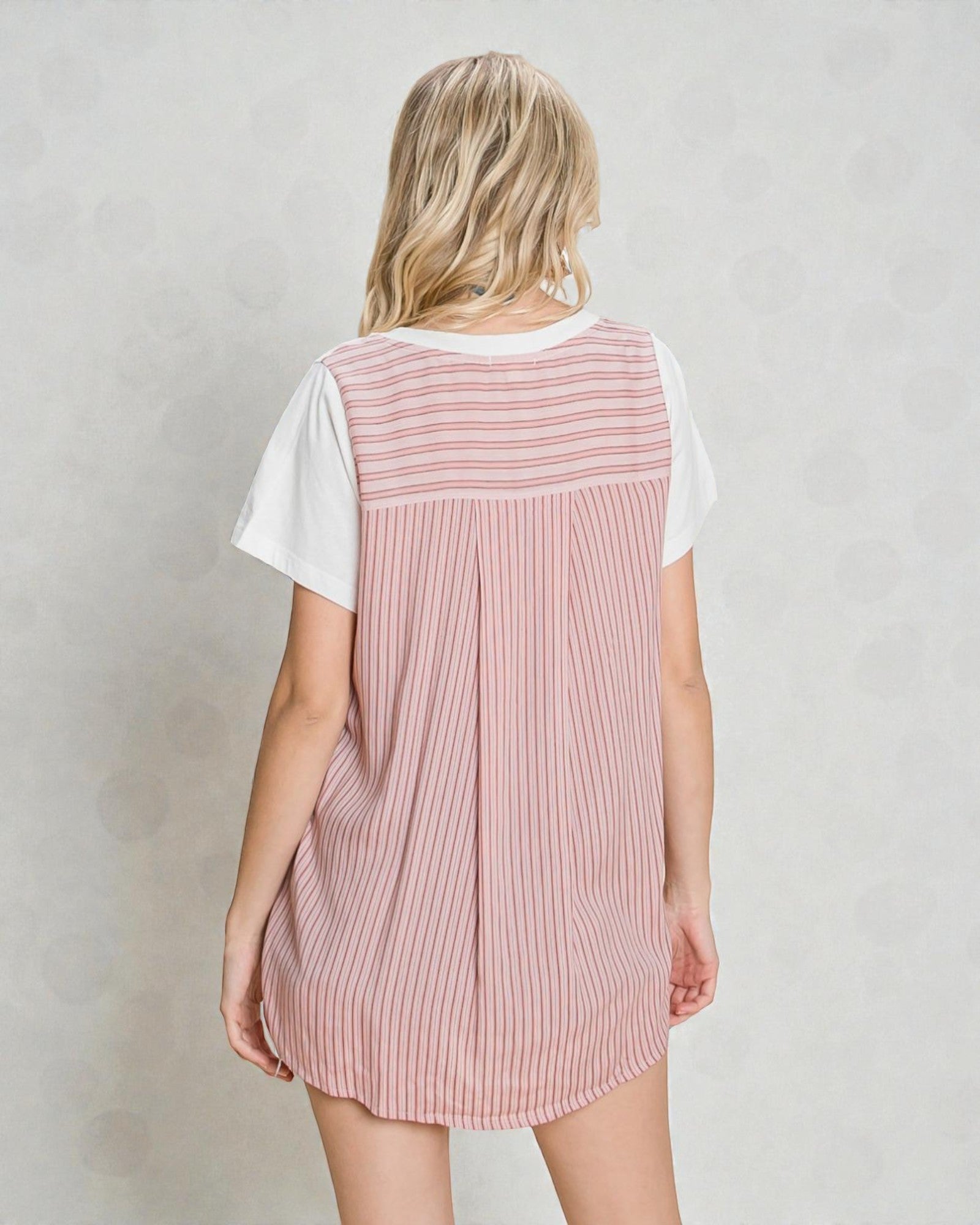 Person wearing a pink striped dress over a white shirt on a plain background