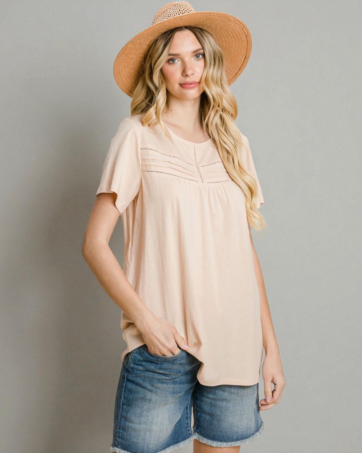 Woman wearing a beige top and denim shorts with a straw hat on a gray background