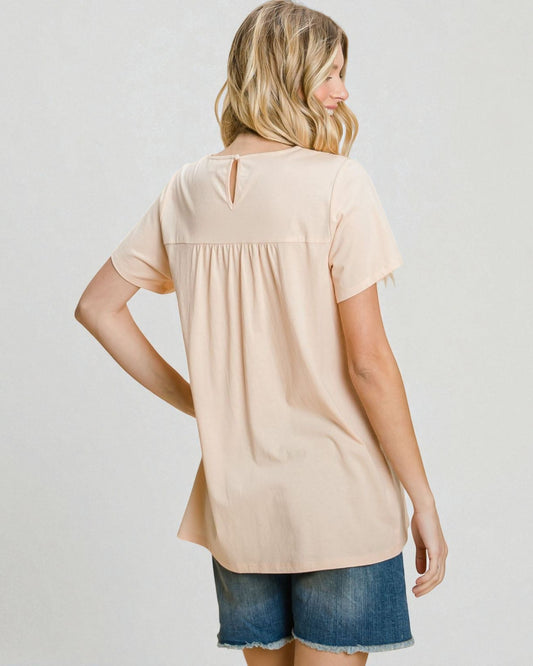 Woman wearing a beige tunic and denim shorts on a plain background