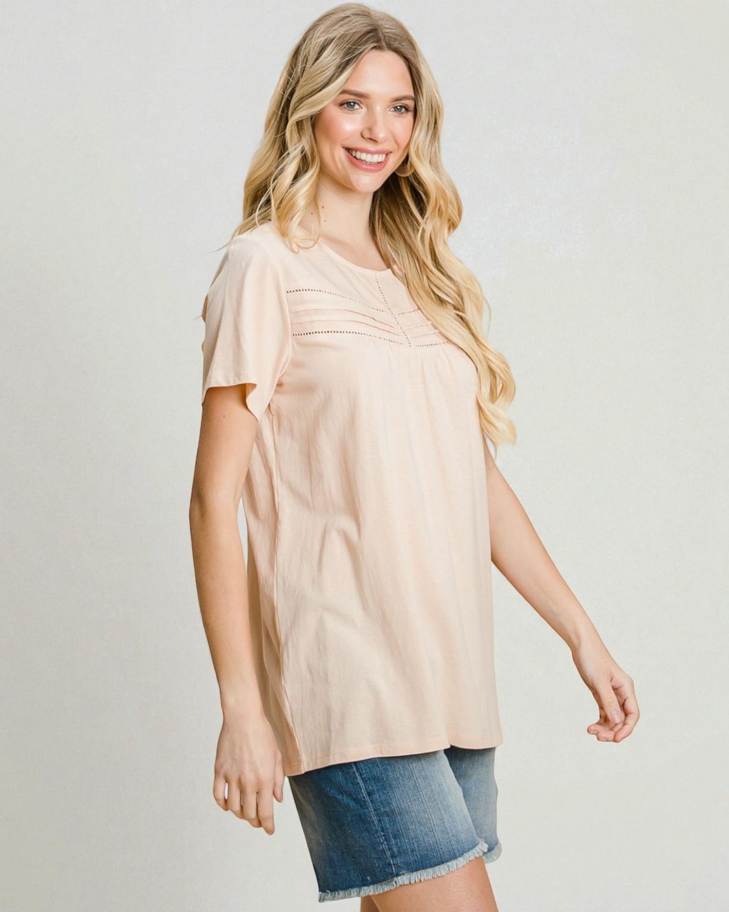 Woman wearing a beige blouse and denim shorts on a plain background