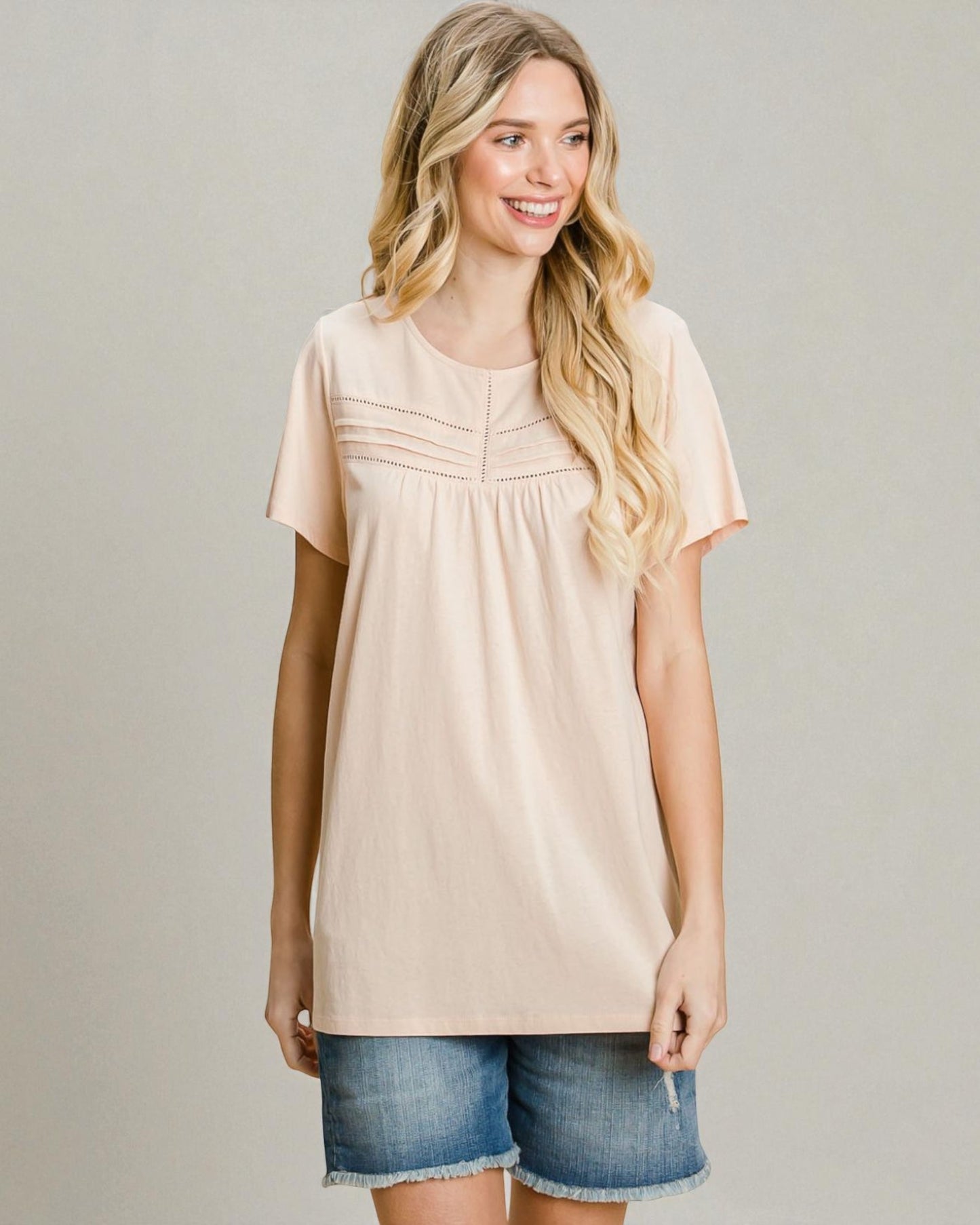 Woman wearing a beige tunic and denim shorts on a plain background