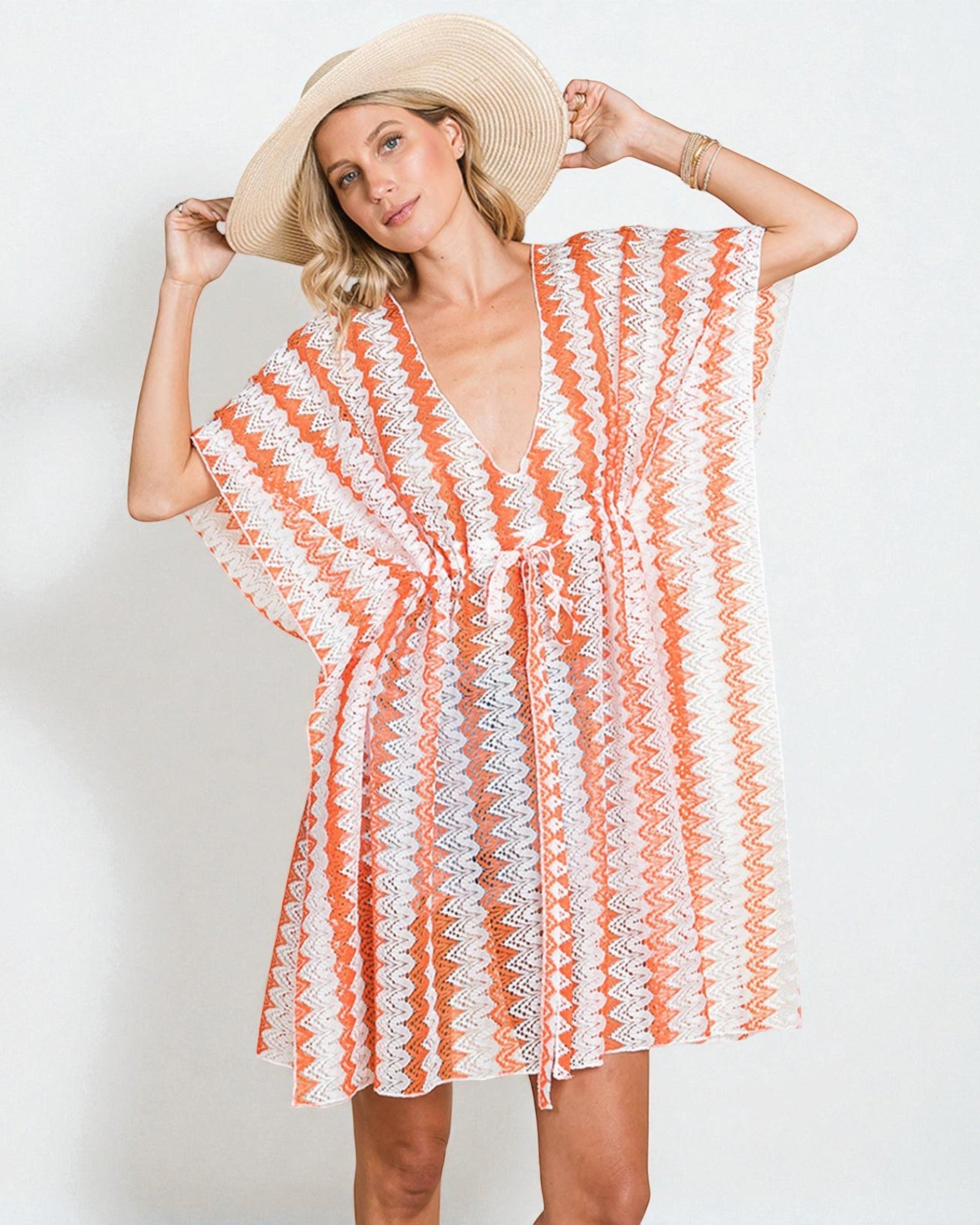 Woman wearing a striped orange and white cover-up with a straw hat on a plain background